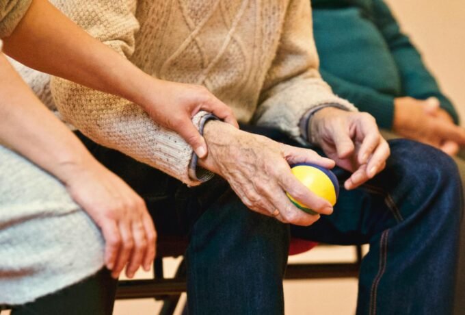 An elderly person receives support from a caregiver, holding hands indoors, showcasing compassion.